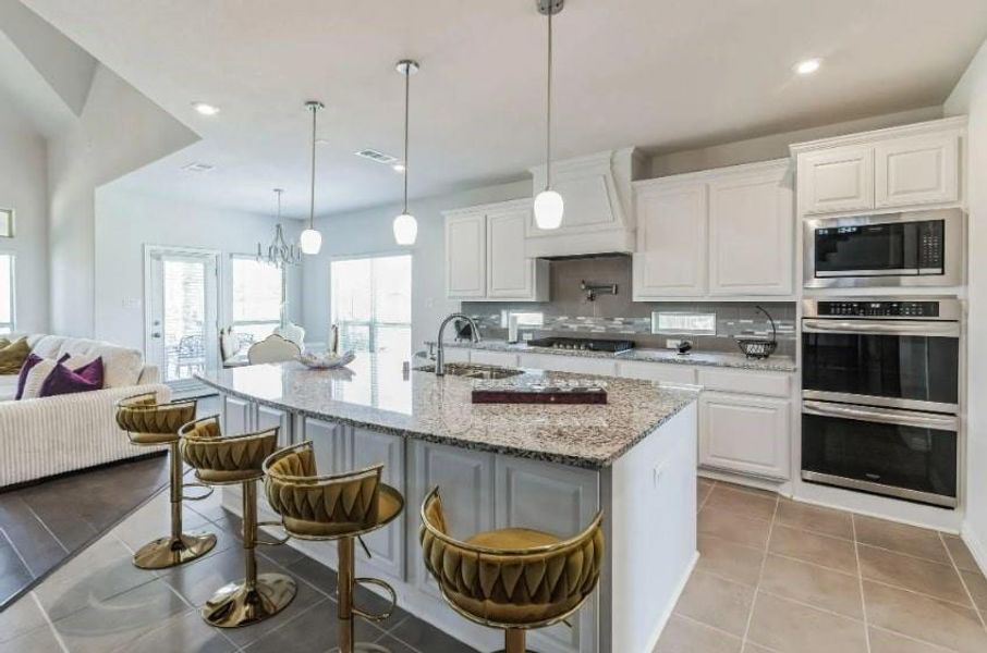 Kitchen featuring light stone countertops, appliances with stainless steel finishes, an island with sink, white cabinets, and light tile patterned flooring