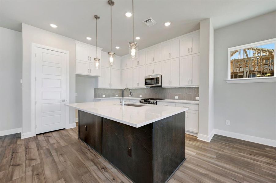 Two tone kitchen with dual tone cabinets, a center island with sink, stainless steel appliances, decorative light fixtures, and dark wood-style flooring