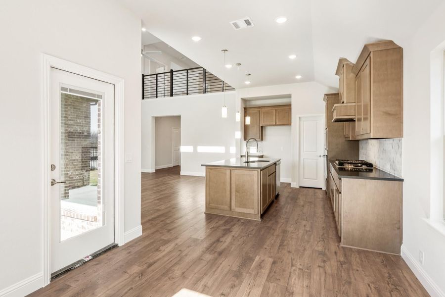 Open kitchen with center island, wood cabinets, dark countertops, and hardwood floors with two-story ceiling above Open kitchen with center island, wood cabinets, dark countertops, and hardwood floors with two-story ceiling above