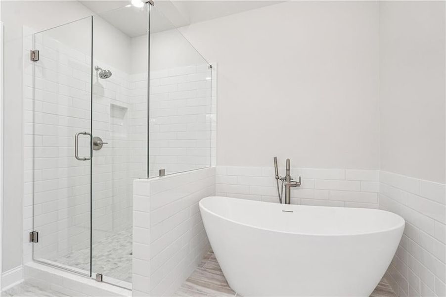 Bathroom featuring a shower stall, tile walls, a soaking tub, and a wainscoted wall