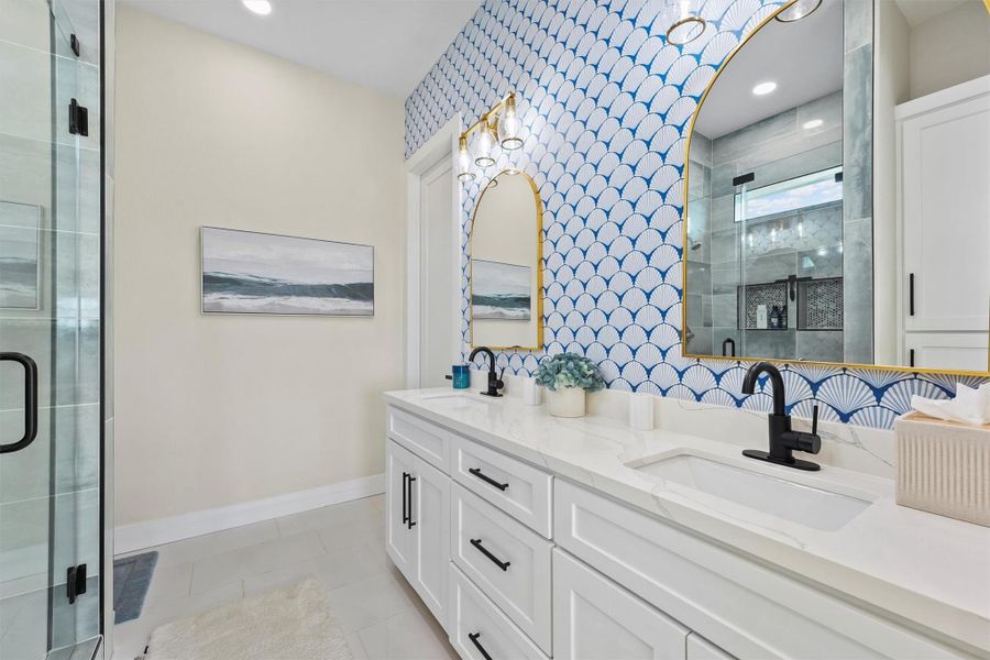 This modern bathroom features a stylish Serena & Lily coastal shell wallpaper over a double vanity with white cabinetry and black fixtures. The walk-in shower offers a glass-roller door. Bright lighting and neutral tones create a fresh, inviting atmosphere.