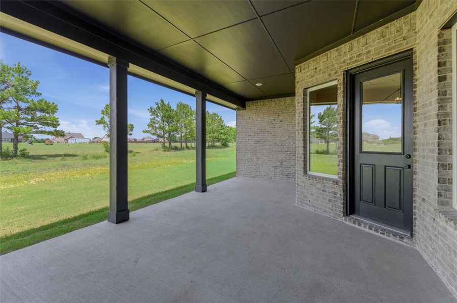 Covered concrete patio featuring brick exterior, black door with glass inserts, and multiple windows Covered concrete patio featuring brick exterior, black door with glass inserts, and multiple windows