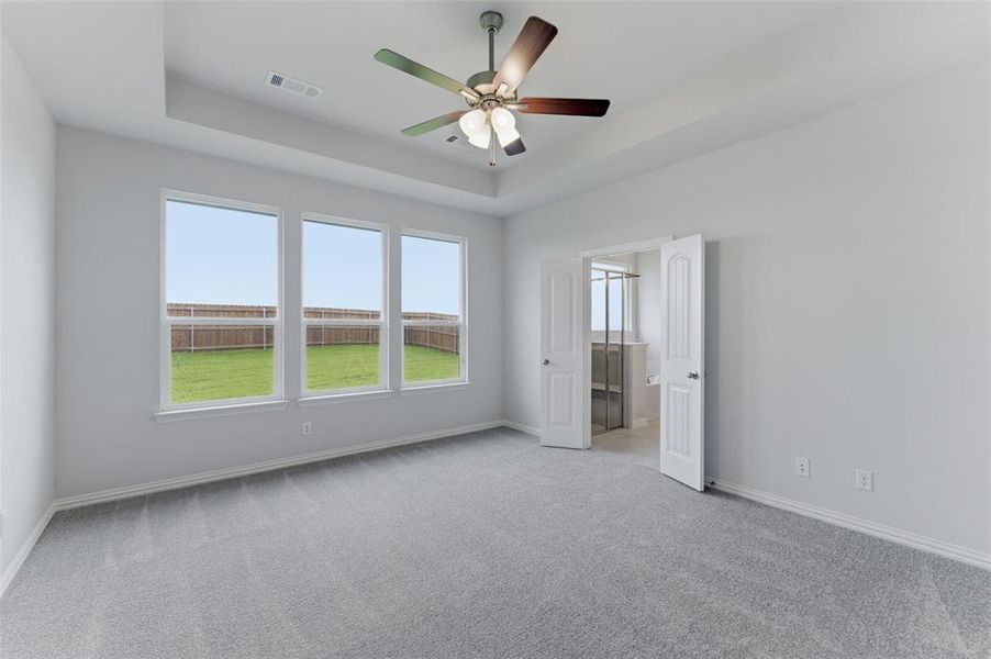 Spacious room with tray ceiling, ceiling fan, and light grey carpeting