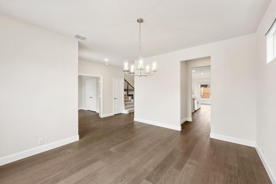 Empty dining room with dark hardwood floors, chandelier, and open view to staircase and kitchen
