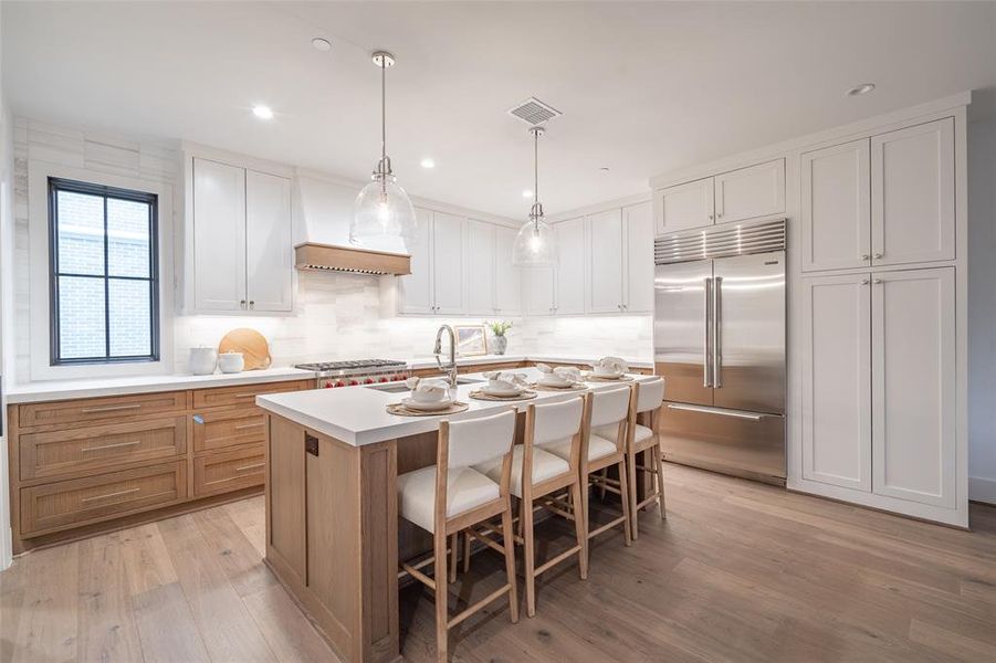 Kitchen with decorative light fixtures, light hardwood / wood-style flooring, a center island with sink, stainless steel appliances, and white cabinets