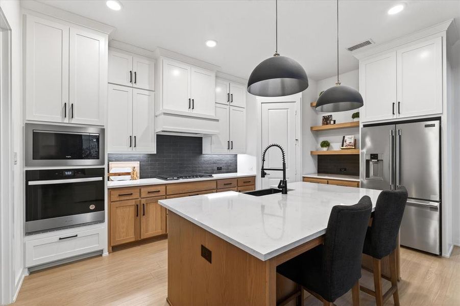 Kitchen with stainless steel appliances, a kitchen bar, brown cabinets, decorative backsplash, and open shelves Kitchen with stainless steel appliances, a kitchen bar, brown cabinets, decorative backsplash, and open shelves