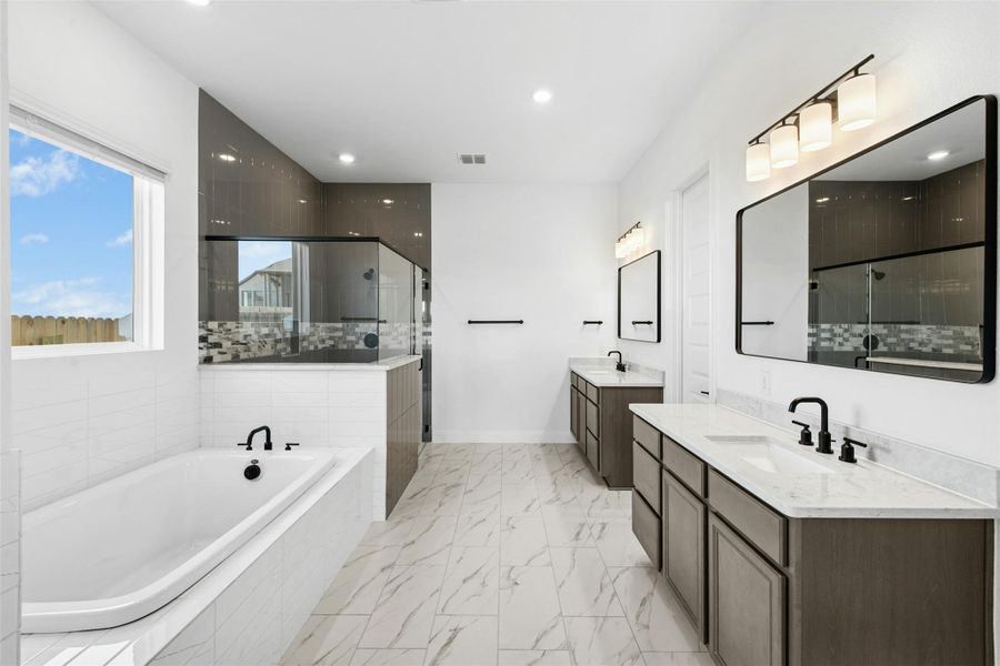 Bathroom featuring two vanities, a bath, a stall shower, light marble finish flooring, and recessed lighting