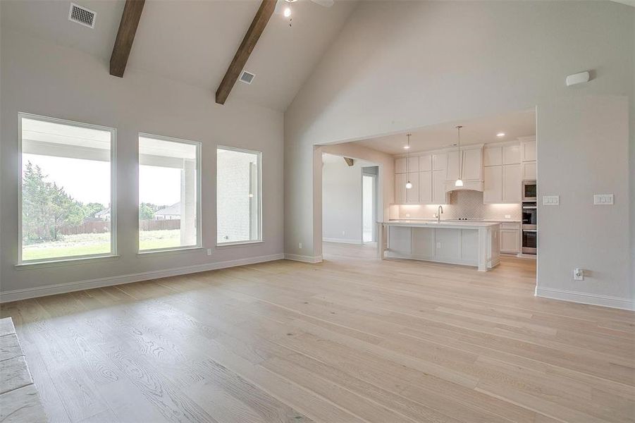 Unfurnished living room featuring sink, beam ceiling, high vaulted ceiling, and light wood-type flooring