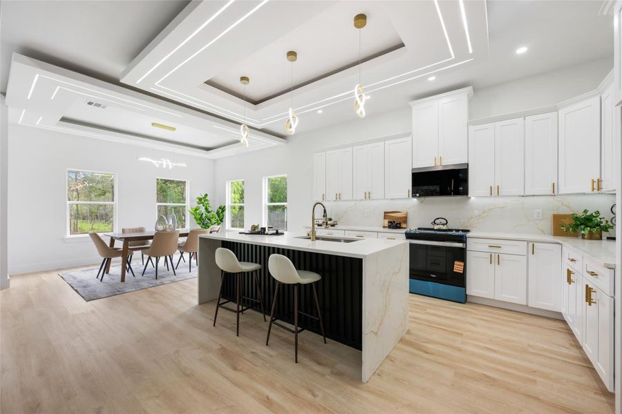 Modern kitchen and dining area featuring light wood-finish flooring, white cabinetry, and gold-tone hardware