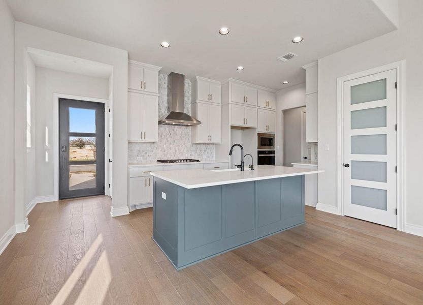 Kitchen featuring light wood finished floors, a sink, stainless steel appliances, tasteful backsplash, and wall chimney range hood Kitchen featuring light wood finished floors, a sink, stainless steel appliances, tasteful backsplash, and wall chimney range hood
