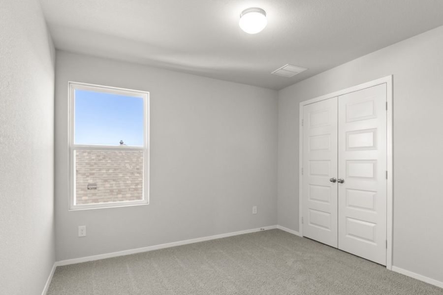 Image of a bedroom with tan carpeting, light grey walls and a window