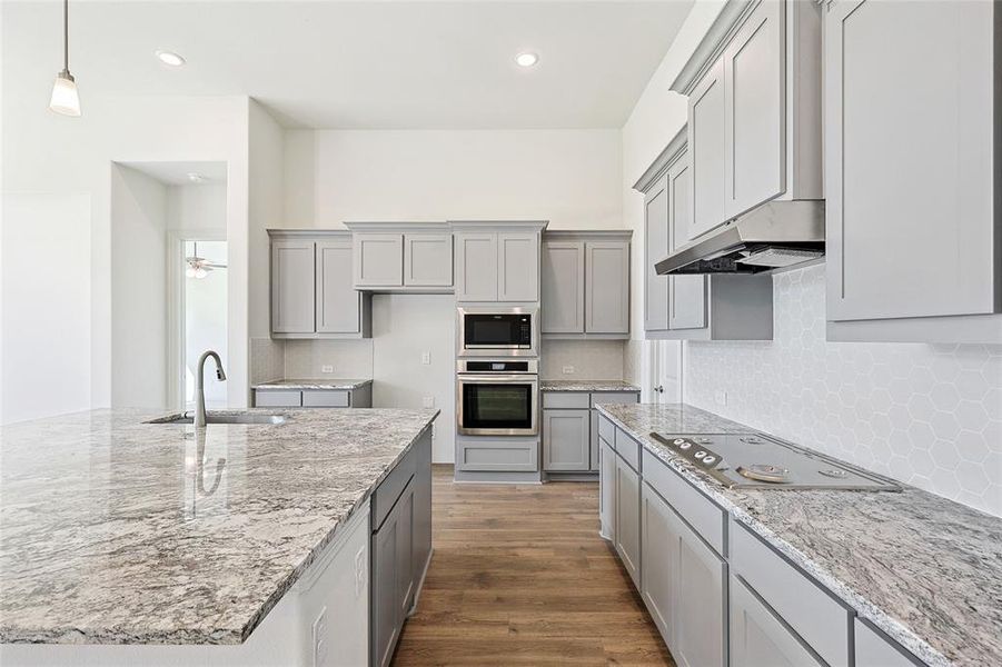 Kitchen with light stone counters, dark wood finished floors, gray cabinets, and tasteful backsplash