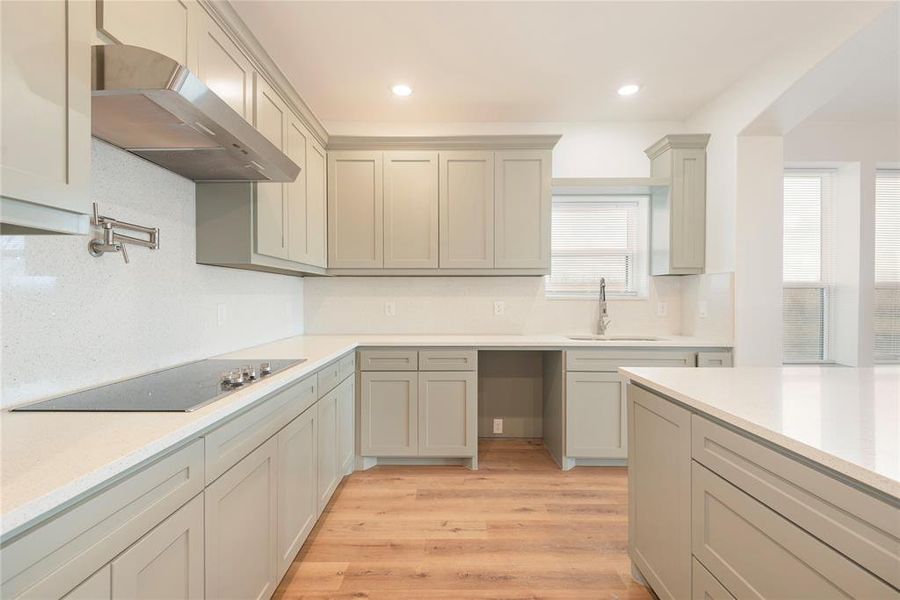 Kitchen with light wood-style floors, under cabinet range hood, decorative backsplash, light stone counters, and recessed lighting