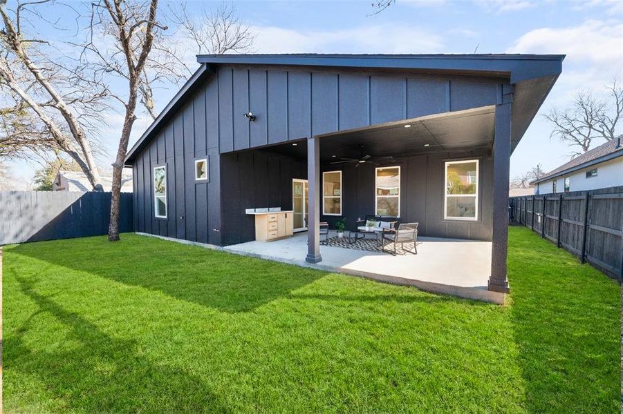Back of house featuring board and batten siding, a fenced backyard, a ceiling fan, and a patio