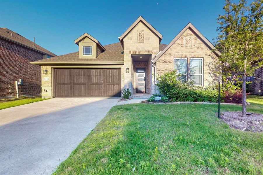 View of front of home with brick siding, a front yard, concrete driveway, and a garage