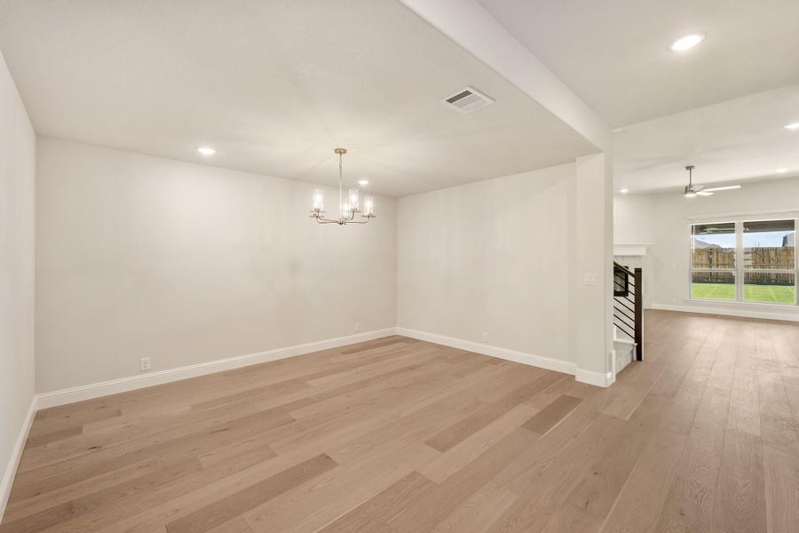 Open dining and living area with light hardwood floors, chandelier, and staircase visible in background Open dining and living area with light hardwood floors, chandelier, and staircase visible in background