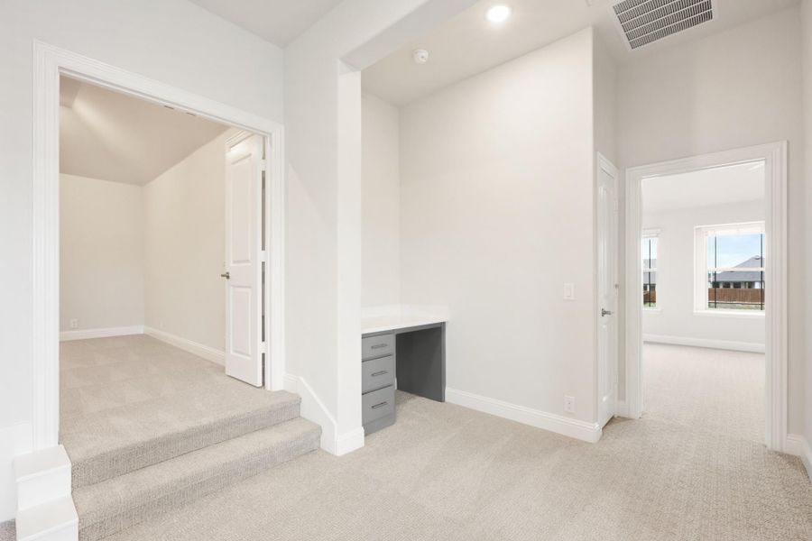 Upstairs hallway with carpet, built-in desk, staircase landing, and doors to adjacent rooms
