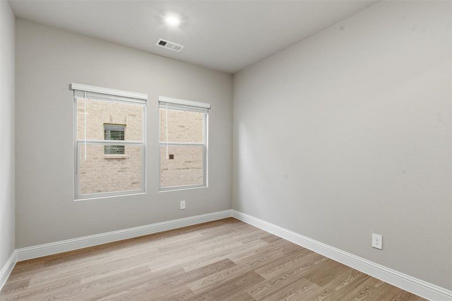 This room features neutral-toned walls, two windows with blinds, and light wood-style flooring