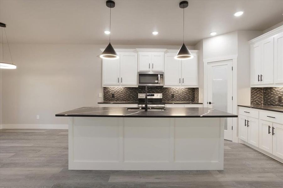 Kitchen featuring light hardwood / wood-style flooring, stainless steel appliances, sink, decorative light fixtures, and white cabinets