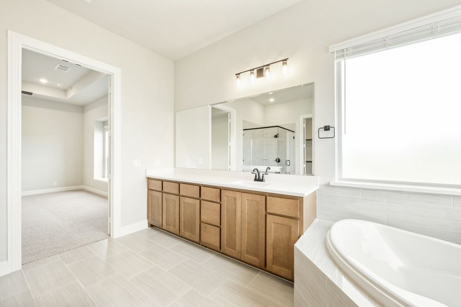Master bathroom with wood vanity, soaking tub, walk-in shower, and large mirror with bar lighting Master bathroom with wood vanity, soaking tub, walk-in shower, and large mirror with bar lighting