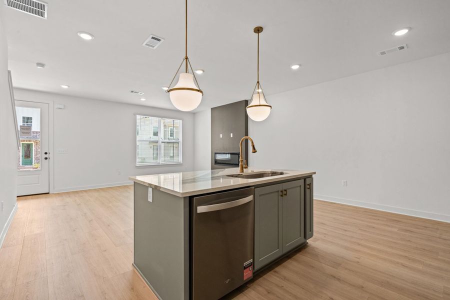 Kitchen island with a built-in sink and dishwasher, complemented by two pendant lights, recessed ceiling lighting, and light wood-finish flooring