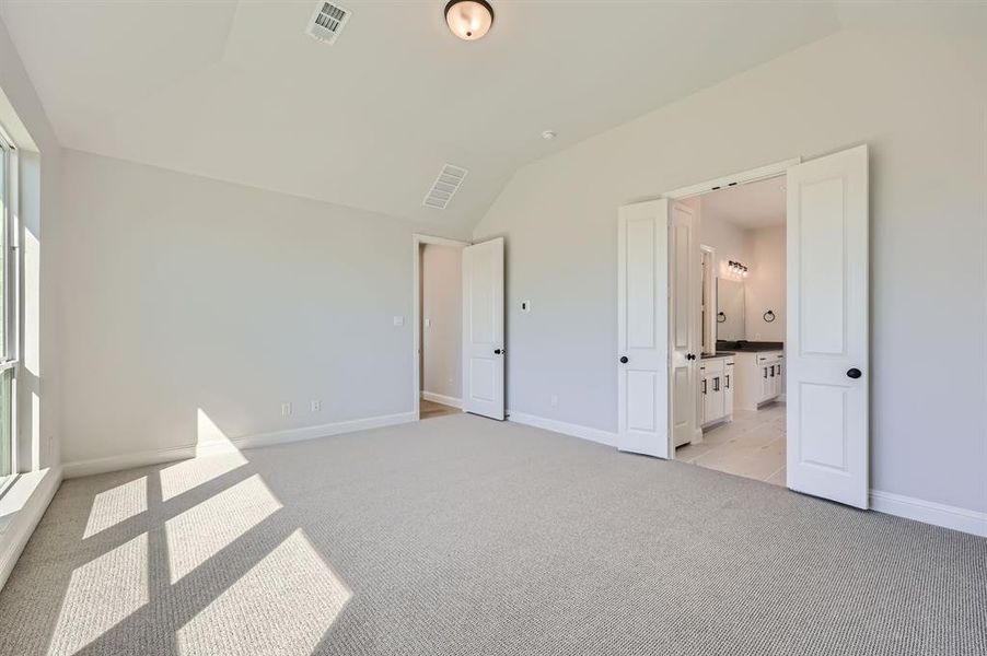 Unfurnished bedroom featuring vaulted ceiling, light carpet, and ensuite bathroom