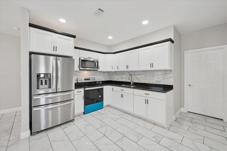 Kitchen with appliances with stainless steel finishes, backsplash, white cabinets, light marble finish floors, and recessed lighting