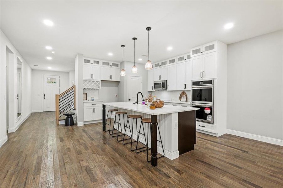 Kitchen with white cabinetry, a breakfast bar, a center island with sink, glass insert cabinets, and recessed lighting