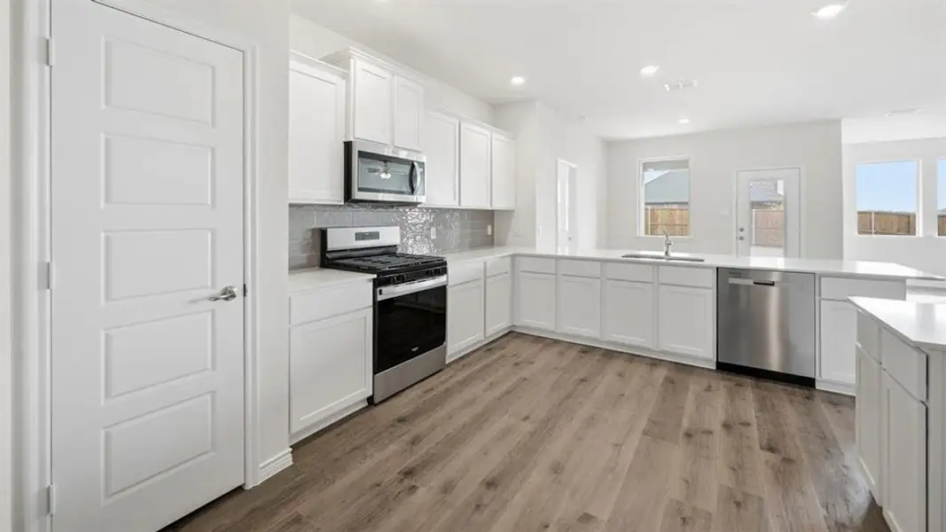 Open-concept kitchen featuring white cabinetry, stainless steel appliances, a tiled backsplash, wood-finish flooring, and ample natural light Open-concept kitchen featuring white cabinetry, stainless steel appliances, a tiled backsplash, wood-finish flooring, and ample natural light