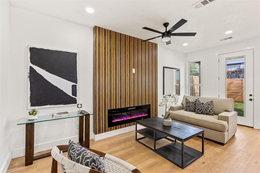 Living room with light wood-type flooring, ceiling fan, a glass covered fireplace, and recessed lighting