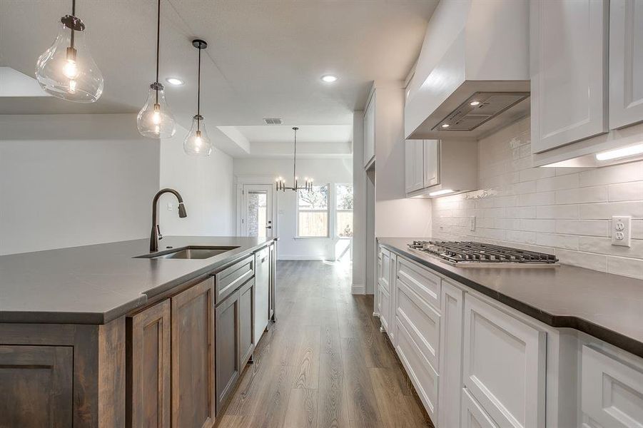 Kitchen with dark countertops, custom exhaust hood, pendant lighting, a chandelier, and dark wood finished floors
