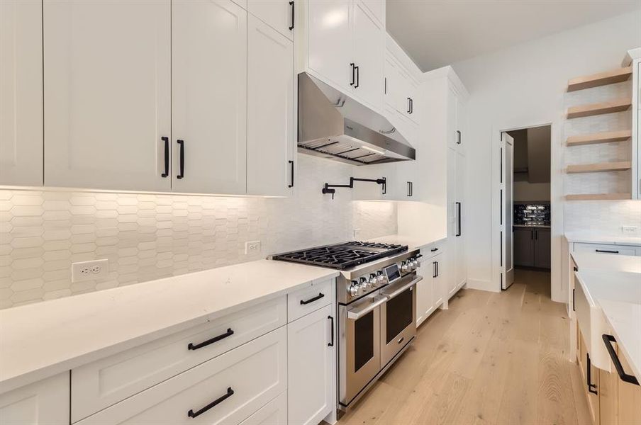 Kitchen featuring white cabinets, range with two ovens, light hardwood / wood-style floors, and decorative backsplash