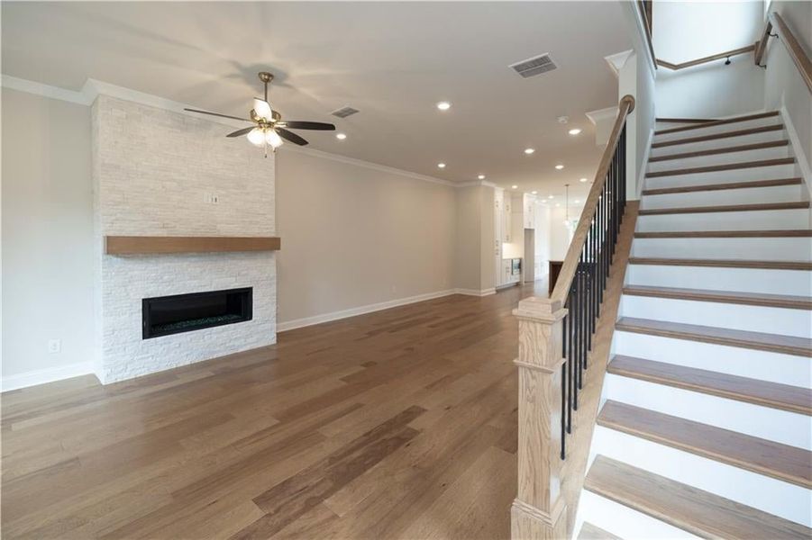 Unfurnished living room featuring crown molding, hardwood / wood-style floors, a stone fireplace, and ceiling fan