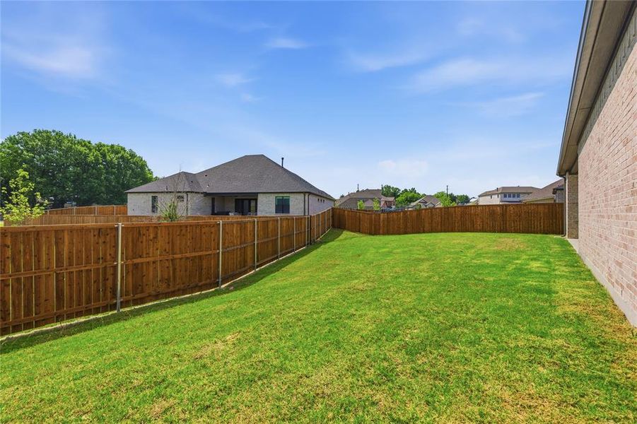 Expansive backyard featuring a green lawn, wood privacy fencing, and a visible portion of the property's brick exterior