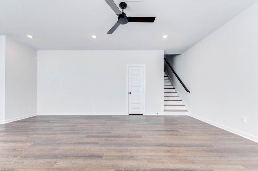 The main living area showcases clean architectural lines, recessed lighting, and a contemporary black ceiling fan that anchors the space. The stairway leads to the upper-level game room and bedrooms, while the door offers convenient storage access perfect for keeping things organized and tidy.