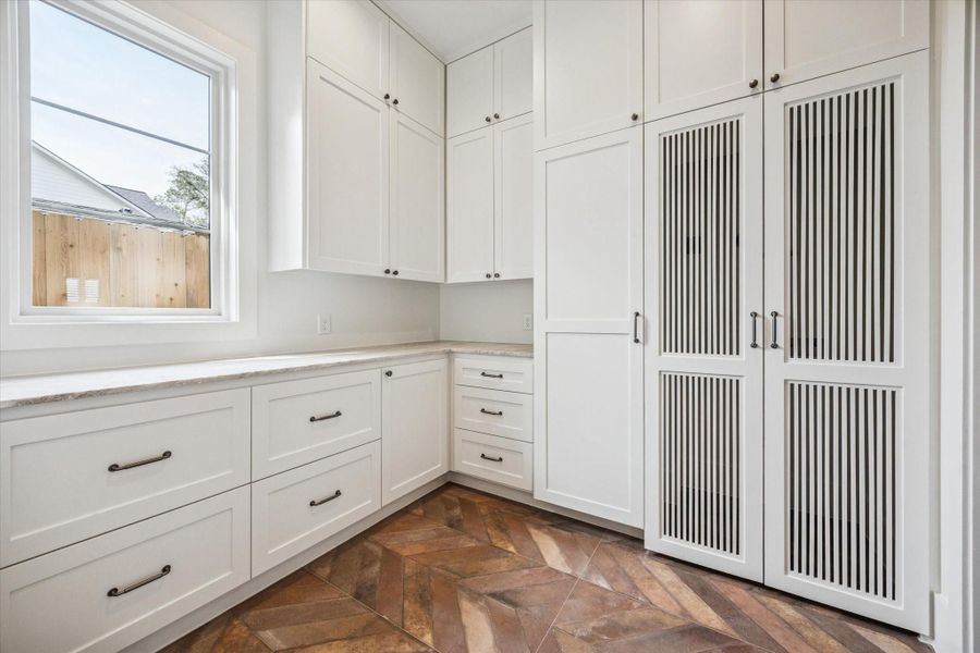 Well appointed utility room with extensive cabinetry, built in folding counter, upper storage, and ventilated cabinet doors, complemented by statement tile flooring and natural light, delivering both functionality and thoughtful design in this Harvard Homes residence.