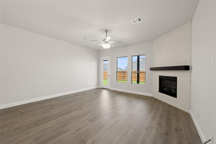 Unfurnished living room with a tiled fireplace, dark wood finished floors, a ceiling fan, and a baseboard heating unit