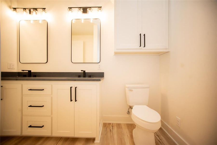 Bathroom with baseboards, double vanity, toilet, wood finished floors, and a sink Bathroom with baseboards, double vanity, toilet, wood finished floors, and a sink