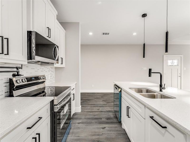 Kitchen featuring pendant lighting, sink, appliances with stainless steel finishes, light stone counters, and white cabinetry