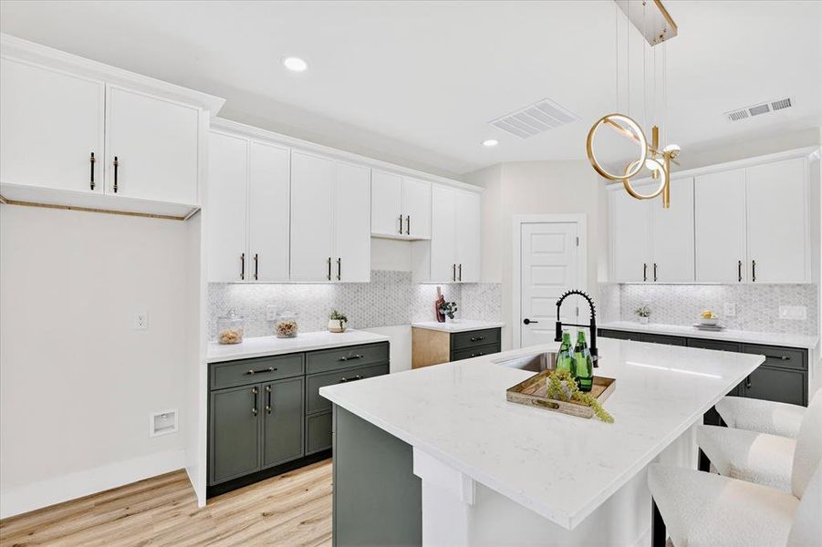 Contemporary kitchen featuring a large central island with a solid surface countertop, two-tone cabinetry with matte black hardware, mosaic tile backsplash, and wood-finish flooring