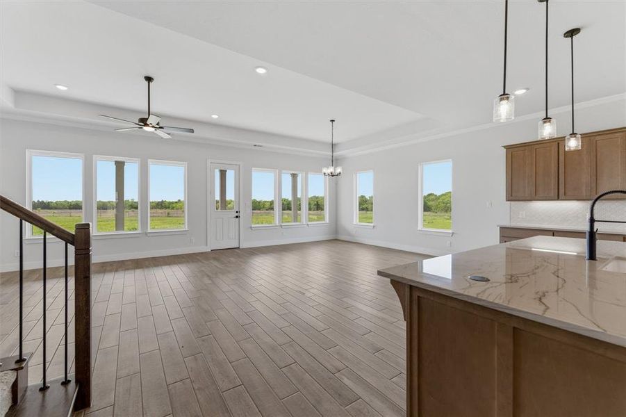 Unfurnished living room with a tray ceiling, wood finish floors, a ceiling fan, plenty of natural light, and suspended lighting