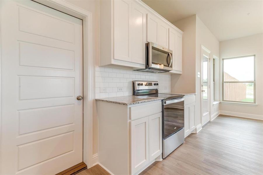Kitchen with stainless steel appliances, tasteful backsplash, light stone countertops, white cabinets, and light wood-type flooring