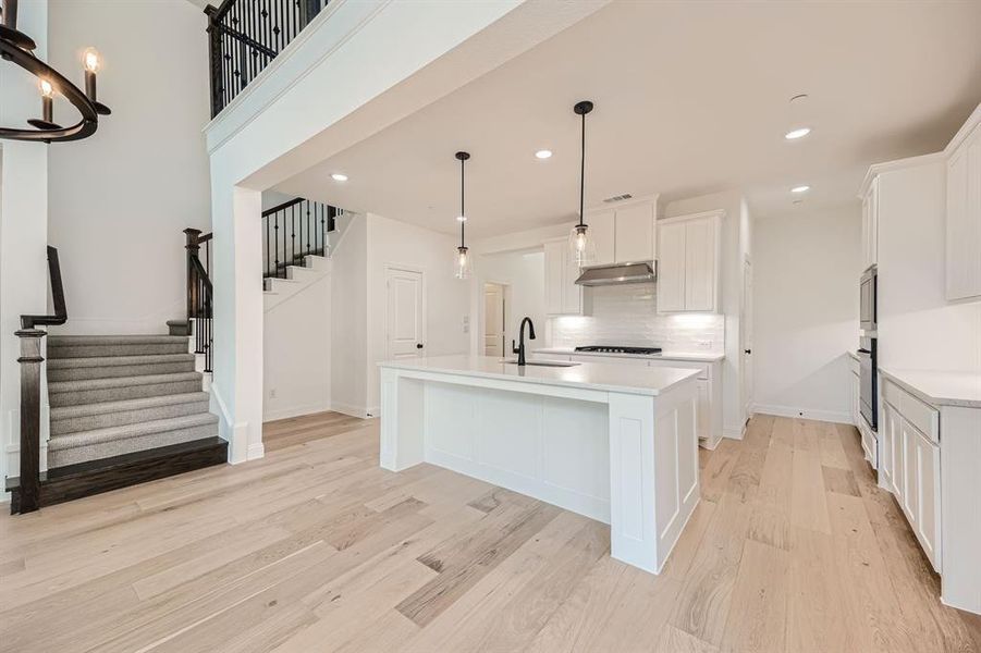 Kitchen with white cabinets, light wood-type flooring, oven, decorative light fixtures, and a center island with sink