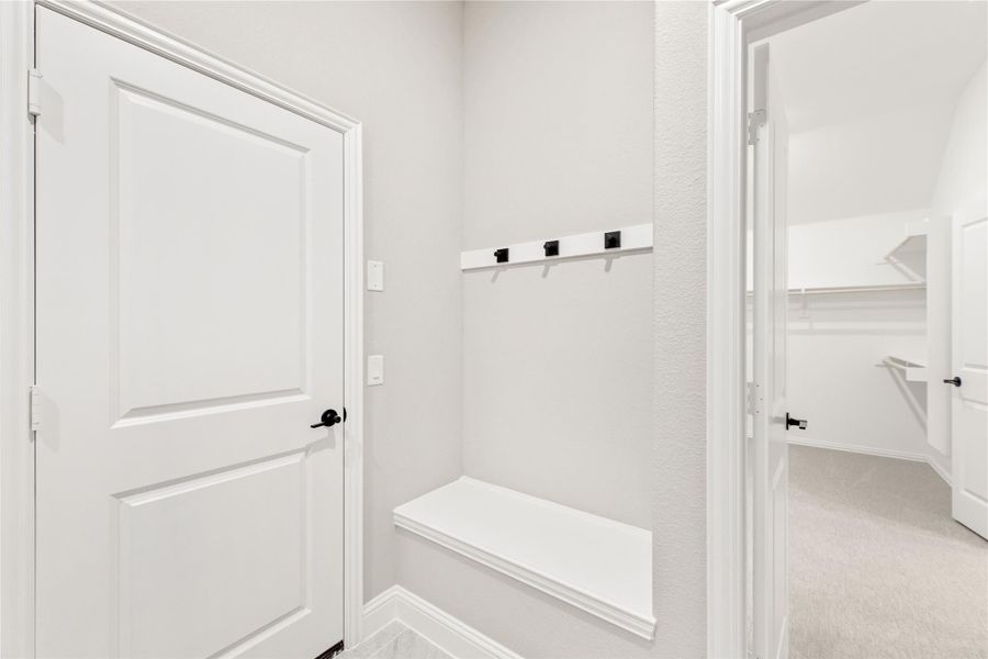 Mudroom area with white bench, wall hooks, and view into walk-in closet with built-in shelving