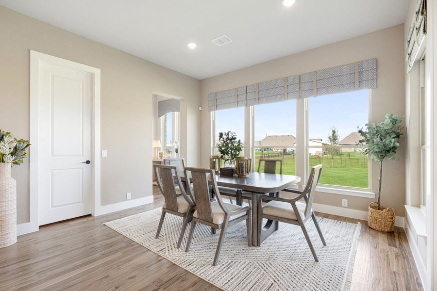 Dining room with wood table, six chairs, hardwood floors, and large windows overlooking a backyard