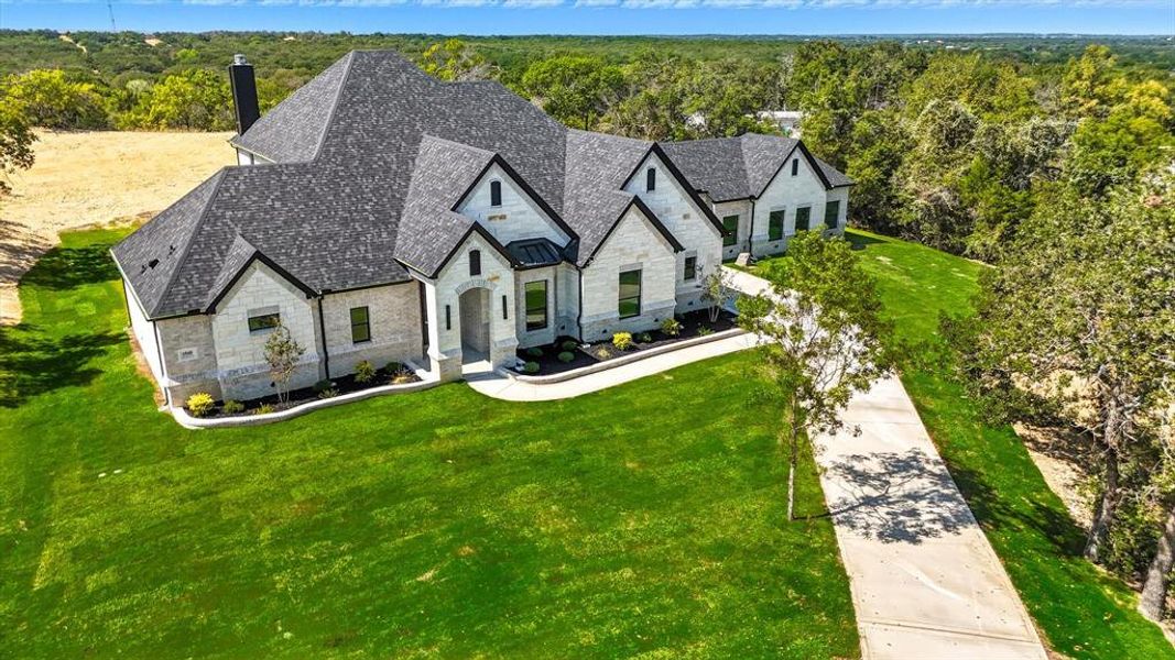 French provincial home featuring stone siding, a front lawn, a chimney, and a forest view