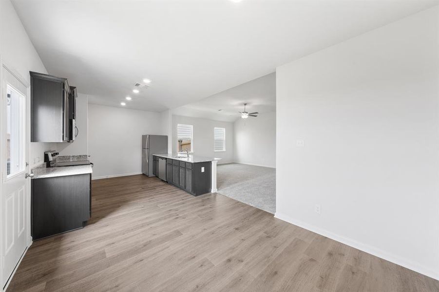 Kitchen with open floor plan, a peninsula, recessed lighting, light stone counters, and light wood finished floors