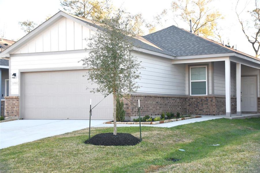 This photo showcases a modern, single-story home with a two-car garage and a charming brick and siding exterior. The property features a well-maintained lawn with a young tree and neat landscaping, providing excellent curb appeal.