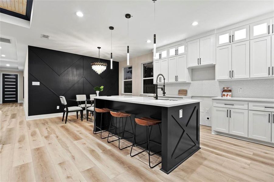Dual tone kitchen with decorative light fixtures, a breakfast bar, glass insert cabinets, a kitchen island with sink, and light wood-style floors Dual tone kitchen with decorative light fixtures, a breakfast bar, glass insert cabinets, a kitchen island with sink, and light wood-style floors