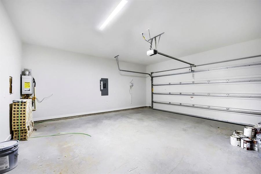 Spacious garage with an overhead automatic garage door opener, concrete flooring, and an exposed electrical panel